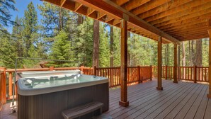 Une terrasse en bois avec un jacuzzi, entourée de grands arbres.
