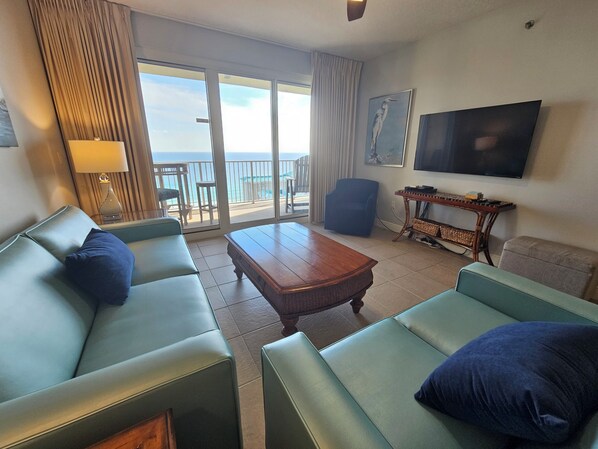 A hotel room with a sofa, a coffee table, a TV, and a balcony with a view.