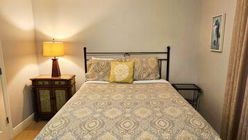 A neatly made bed with a patterned bedspread and two pillows, a bedside table with a lamp, and a framed picture on the wall.
