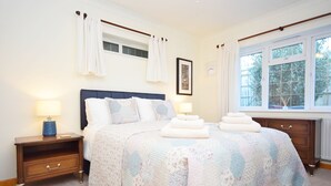 A neatly arranged bedroom with a large bed, two bedside tables, a window with curtains, and a framed picture on the wall. - Little Crossways , Goodwood -  an annexe that sleeps 2 guests  in 1 bedroom (Chichester)