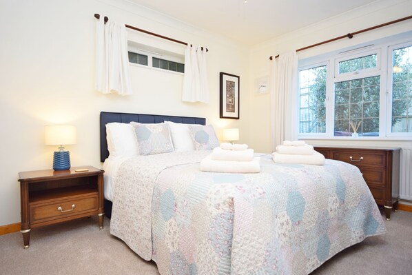 A neatly arranged bedroom with a large bed, two bedside tables, a window with curtains, and a framed picture on the wall.