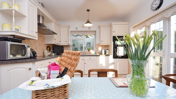 A kitchen with white cabinets, a microwave, a wicker basket, and a vase with green plants on a blue table. - Little Crossways , Goodwood -  an annexe that sleeps 2 guests  in 1 bedroom (Chichester)
