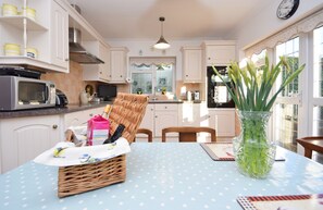 A kitchen with white cabinets, a microwave, a wicker basket, and a vase with green plants on a blue table.