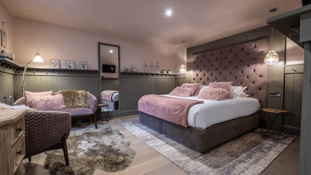 A bedroom with a large bed, a chair, a dresser, and a mirror.