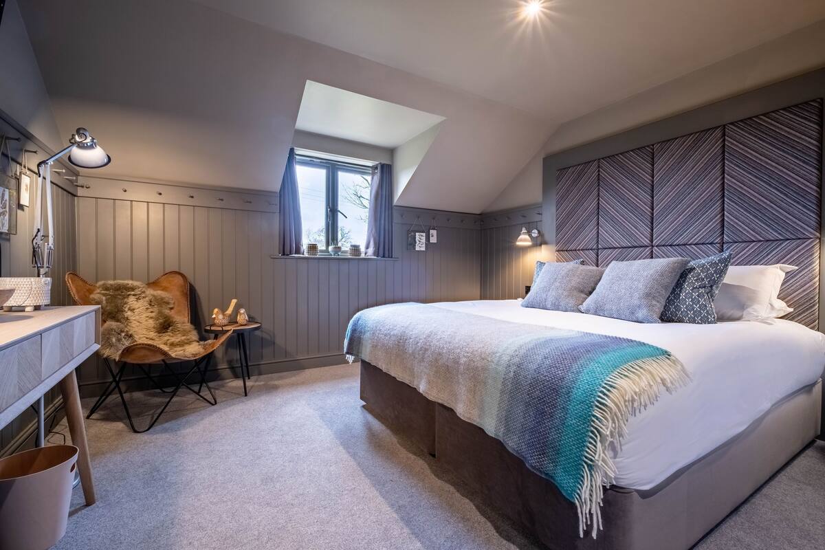 Une chambre à coucher comprenant un lit, un bureau, une chaise, une fenêtre et un plafond en pente.