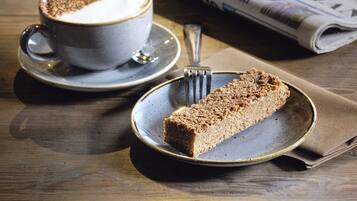 A table with a cup of coffee, a slice of cake, and a newspaper.