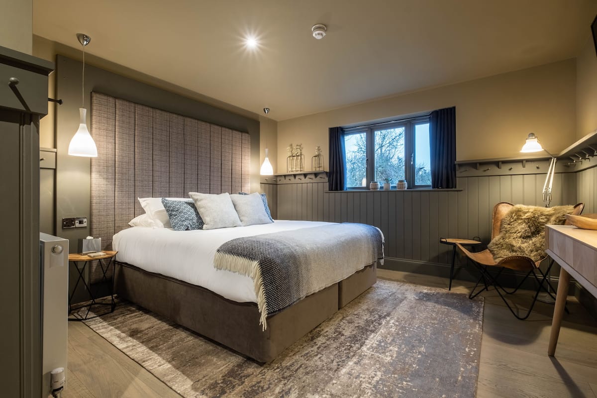 Une chambre à coucher avec un grand lit, des tables de chevet, un bureau et une fenêtre avec des rideaux.