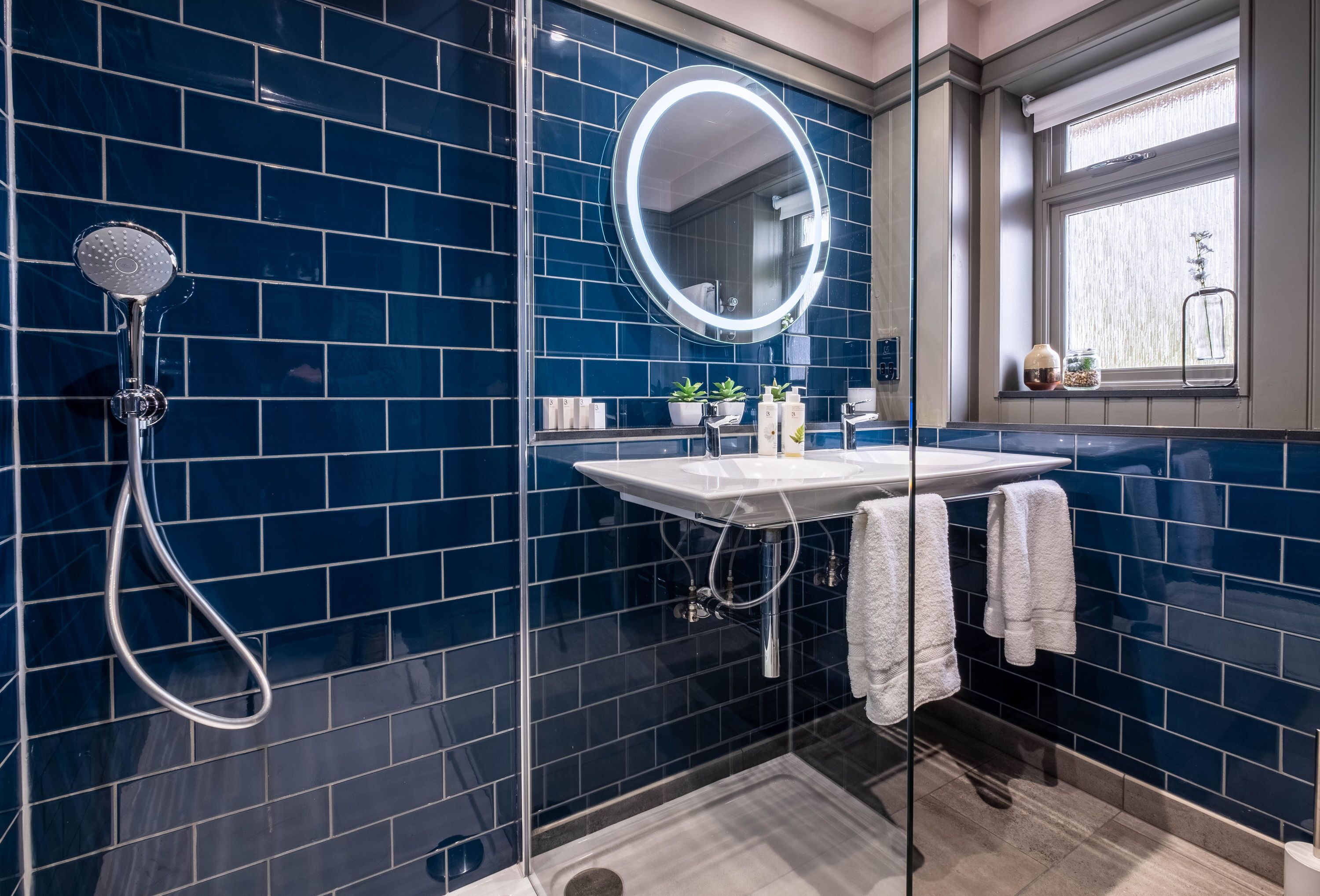 Un baño con ducha de vidrio, un lavamanos blanco con espejo y una ventana con vistas al exterior.