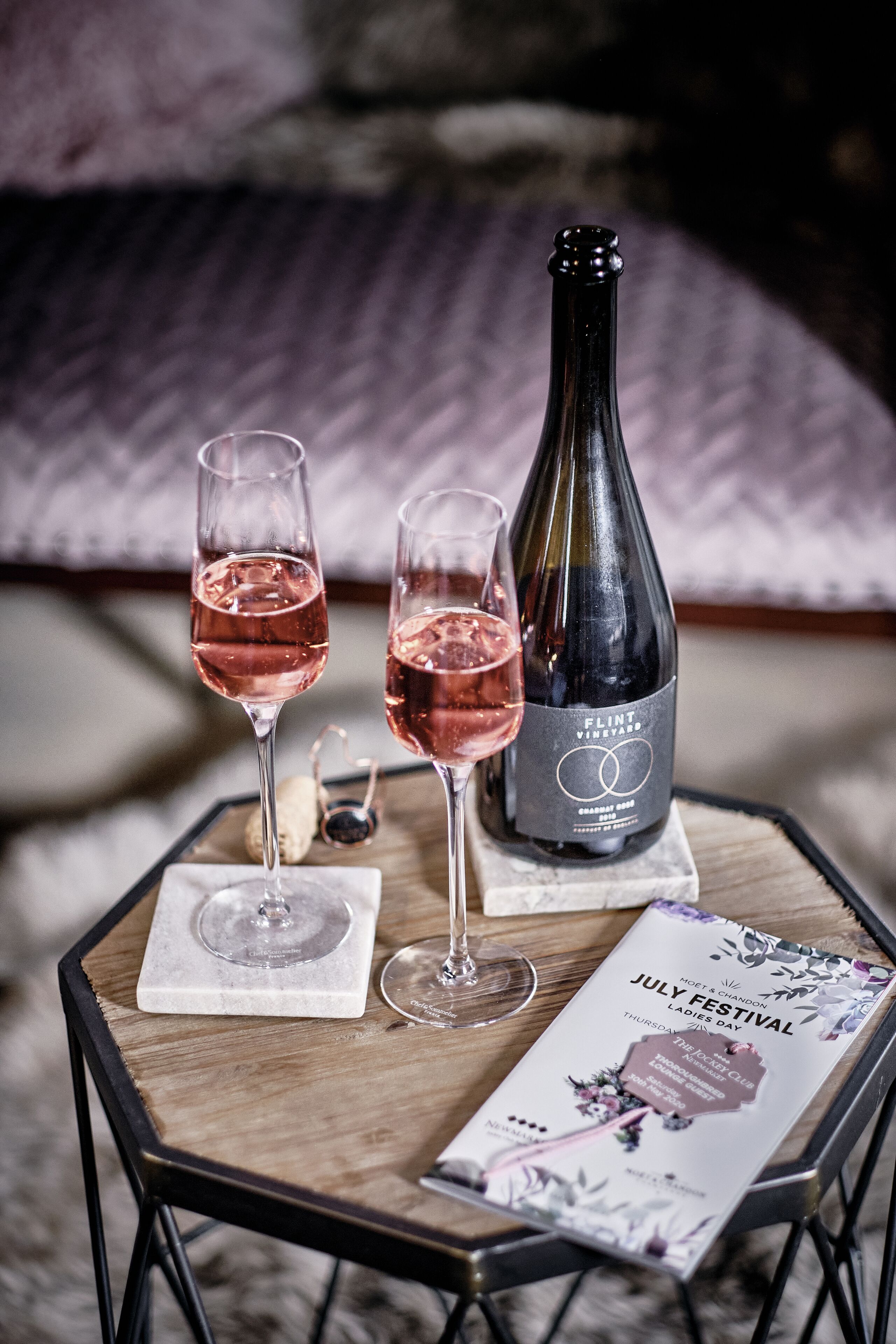 A table with two glasses of rosé wine, a bottle of wine, and a brochure for a July festival.