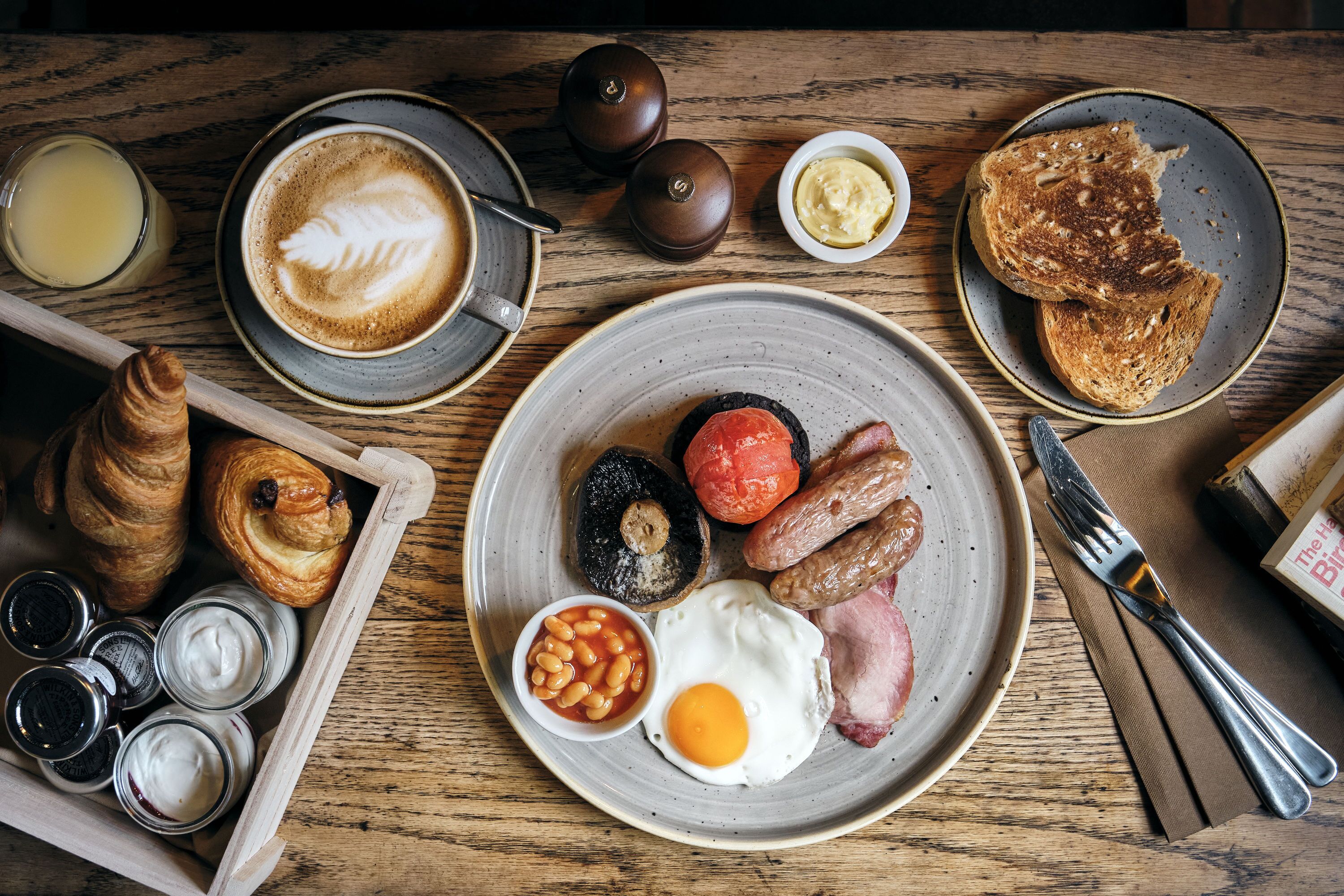 A breakfast setting with croissants, eggs, sausages, and toast on a wooden table.