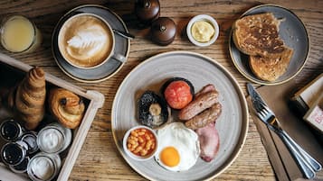 A breakfast setting with croissants, eggs, sausages, and toast on a wooden table.