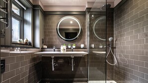 A modern bathroom with two sinks, a large mirror, and a glass-enclosed shower.