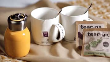 A bed with a beige blanket, two white mugs, a yellow thermos, and a package of teapigs peppermint leaves.
