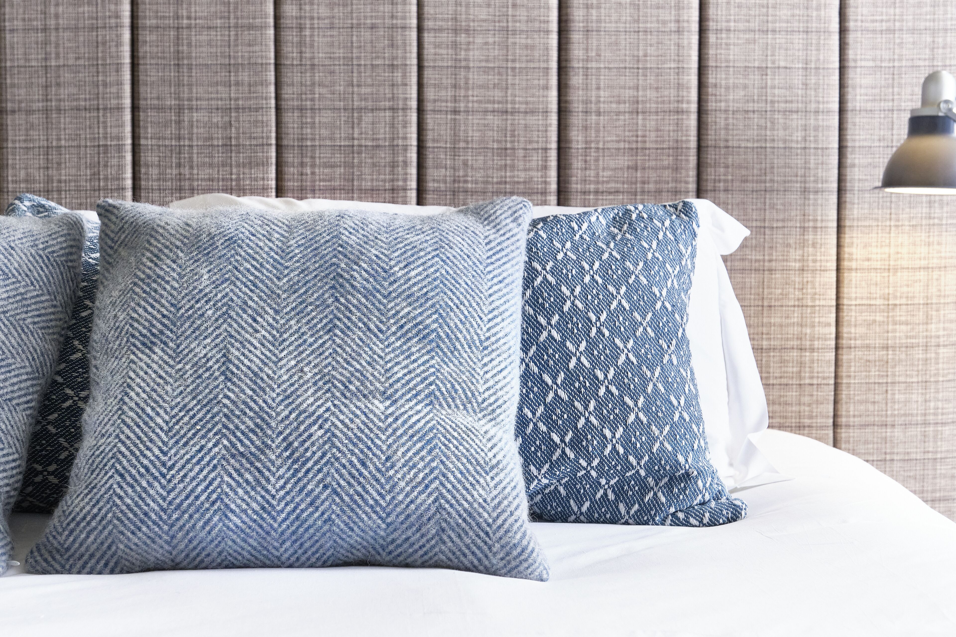 Una cama con tres almohadas, un cabecero y una lámpara de pared.