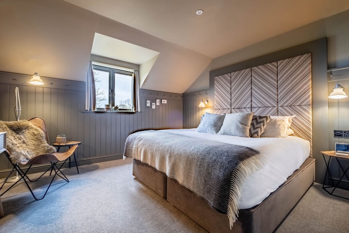 Une chambre avec un grand lit, une chaise, une petite table et une fenêtre.