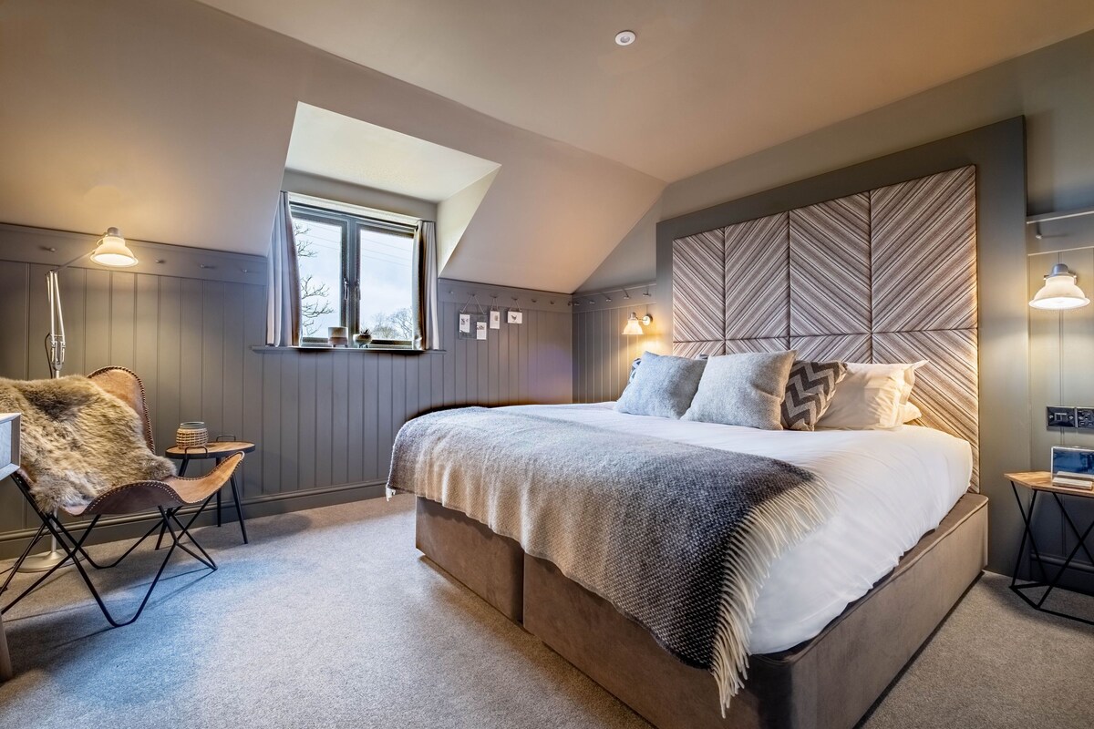 Une chambre à coucher avec un grand lit, une lucarne, une chaise et une table de chevet.