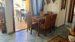 Un coin repas avec une table en bois et des chaises en osier, un tapis à motifs et des œuvres d’art décoratives accrochées au mur.