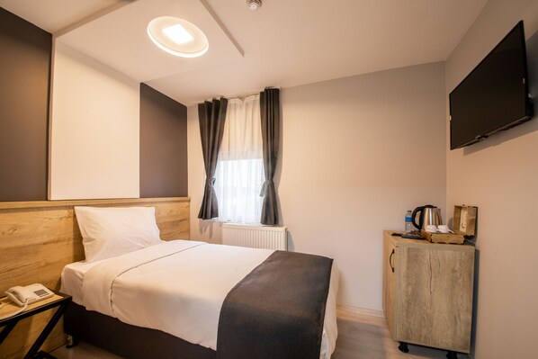 Una habitación de hotel con cama, mesita de noche, un armario de madera, televisor y ventana con cortinas.