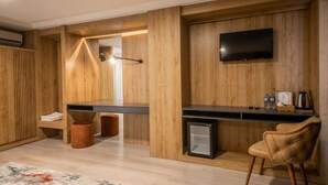 Et moderne værelse med træpaneler, et fladskærms-tv, et lille køleskab, en stol og et skrivebord med en lampe.