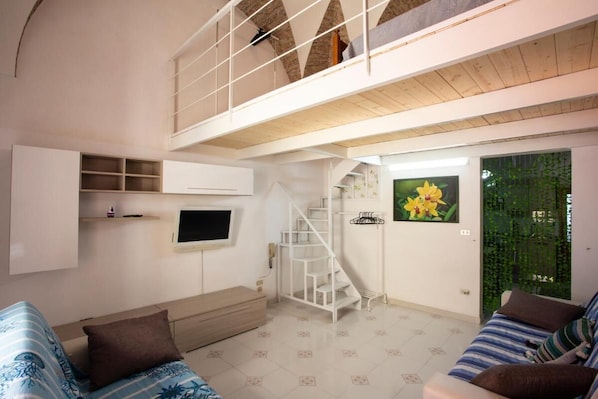 Un vaste espace de vie doté d’un haut plafond, d’un escalier, d’un téléviseur à écran plat et d’un mur végétal.