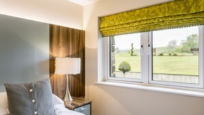 Un dormitorio con cama, mesita de noche, lámpara y ventana con vista a un jardín.