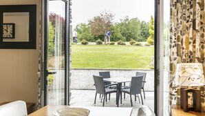Un área de comedor con una mesa y sillas, un tazón sobre la mesa, y vistas a un jardín donde alguien cuida las plantas.