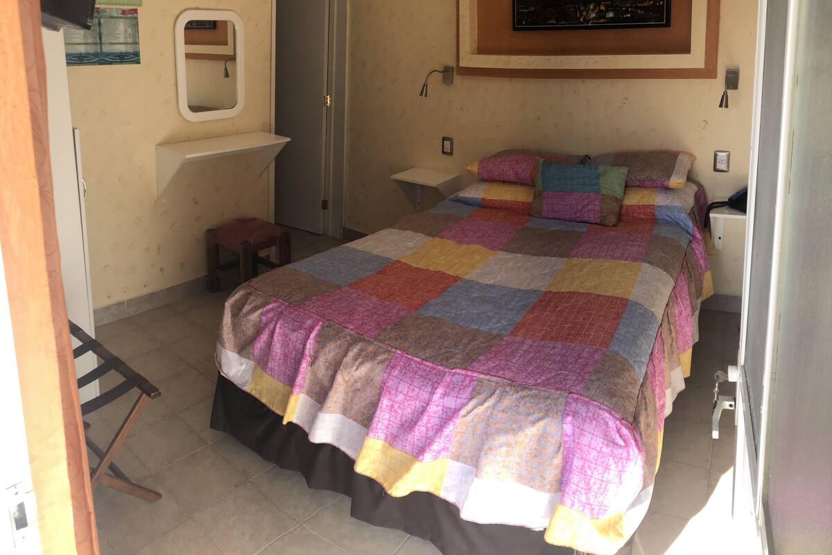 Een slaapkamer met een groot bed, nachtkastje, spiegel en een deur.