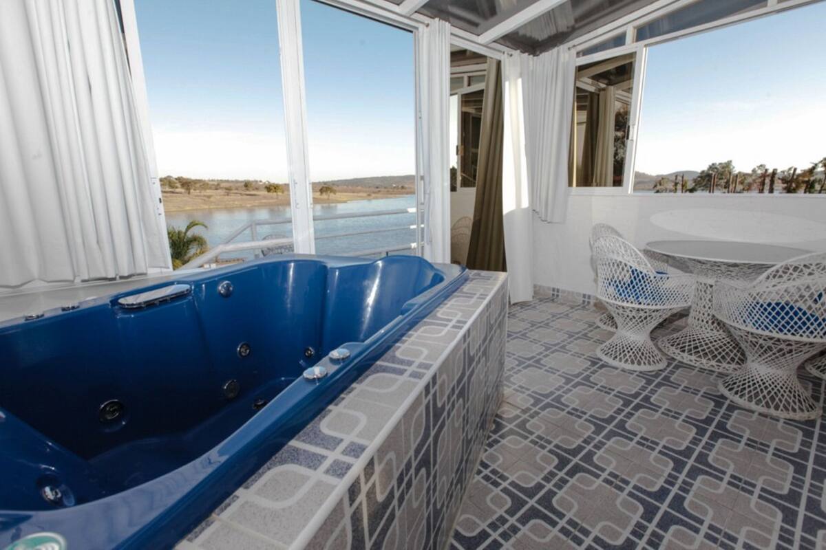 Een kamer met een groot blauw jacuzzi, een patroon vloer en uitzicht op water en heuvels.