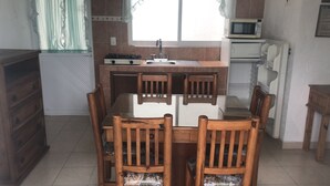 Una cocina compacta con una mesa y sillas, estufa, lavamanos y microondas.