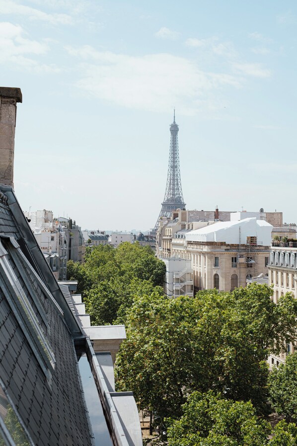 A view of the Eiffel Tower from a building with a modern architectural design, surrounded by lush green trees. - Rooftop Views of the Arc de Triomphe, by Veeve (Paris)