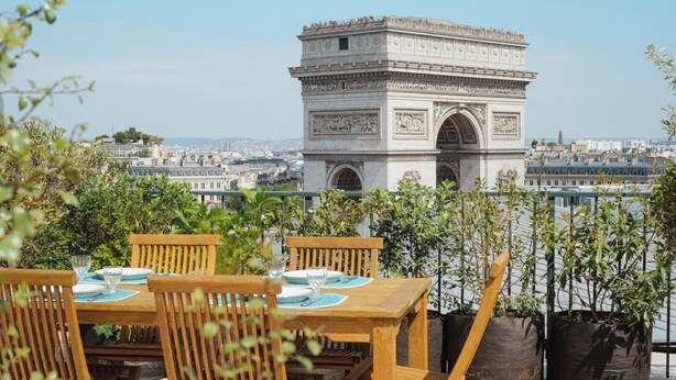 A terrace with a view of the Arc de Triomphe, wooden furniture, and potted plants. - Rooftop Views of the Arc de Triomphe, by Veeve (Paris)