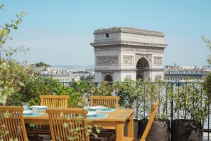 A terrace with a view of the Arc de Triomphe, wooden furniture, and potted plants. - Rooftop Views of the Arc de Triomphe, by Veeve (Paris)