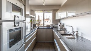 A modern kitchen with stainless steel appliances, a large window, and a view of the city. - Rooftop Views of the Arc de Triomphe, by Veeve (Paris)