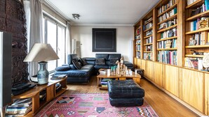 A living room with a sectional sofa, a coffee table, a bookshelf, and a patterned rug. - Rooftop Views of the Arc de Triomphe, by Veeve (Paris)
