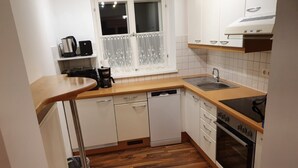 A compact kitchen with white cabinets, a wooden countertop, a dishwasher, a sink, and a stove. - Haus Kampl - Apartment Aussee (Pichl-Kainisch)