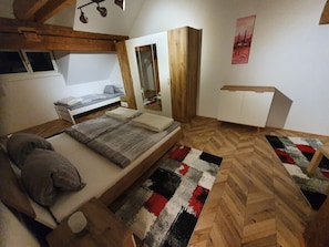 Une chambre à coucher comprenant un lit, une table de chevet, une armoire, un miroir et un parquet en bois à motifs chevrons.