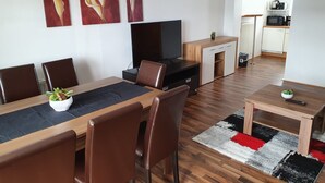 A modern living room with a dining area, a TV, and a kitchen in the background. - Haus Kampl - Apartment Aussee (Pichl-Kainisch)