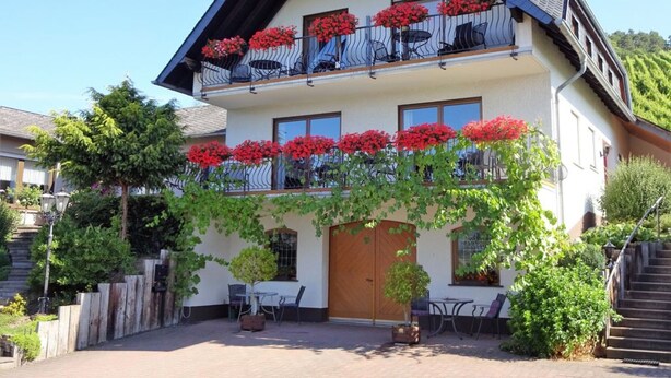 A two-story house with a balcony adorned with red flowers, a wooden door, and a small patio area with outdoor furniture. - Well-kept vacation home in the middle of the vineyards, apartment 2, short vacation on request (Osann)