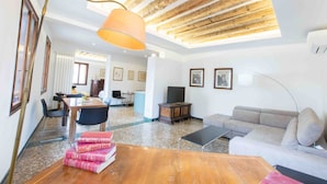 A spacious living area with a wooden ceiling, a sofa, a coffee table, and a dining area with chairs and a table.