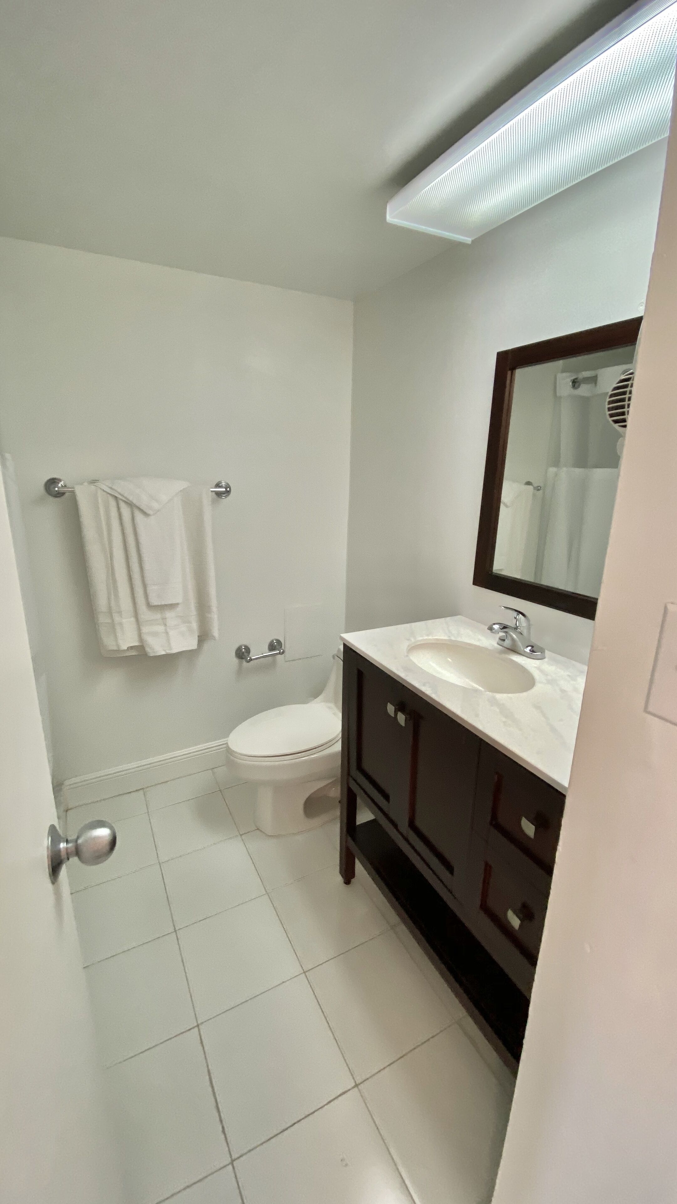 A bathroom with a toilet, sink, and mirror. There is a towel rack with a towel hanging on it. The floor is tiled.