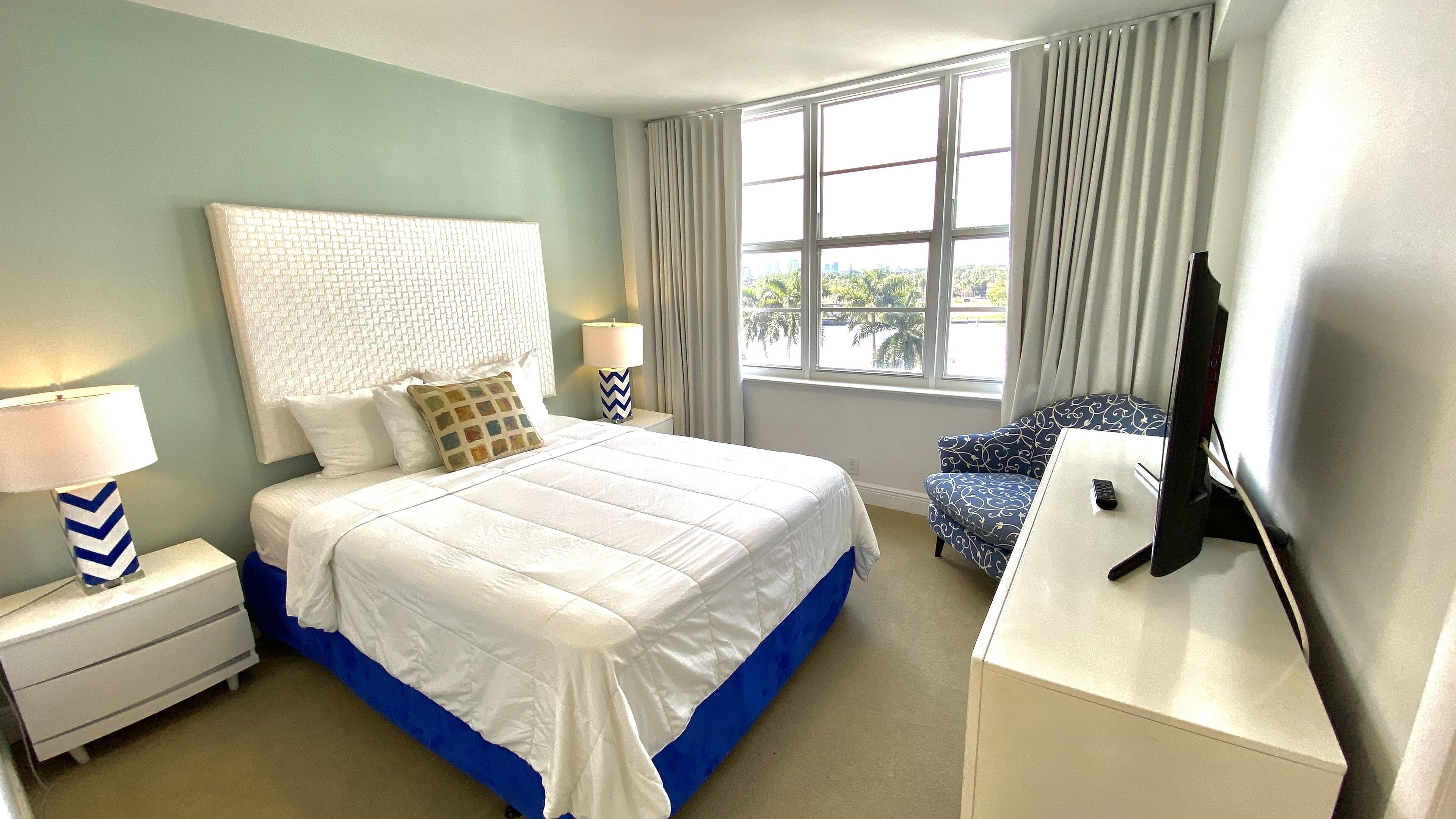 A hotel room with a large bed, a desk, a chair, and a TV.
