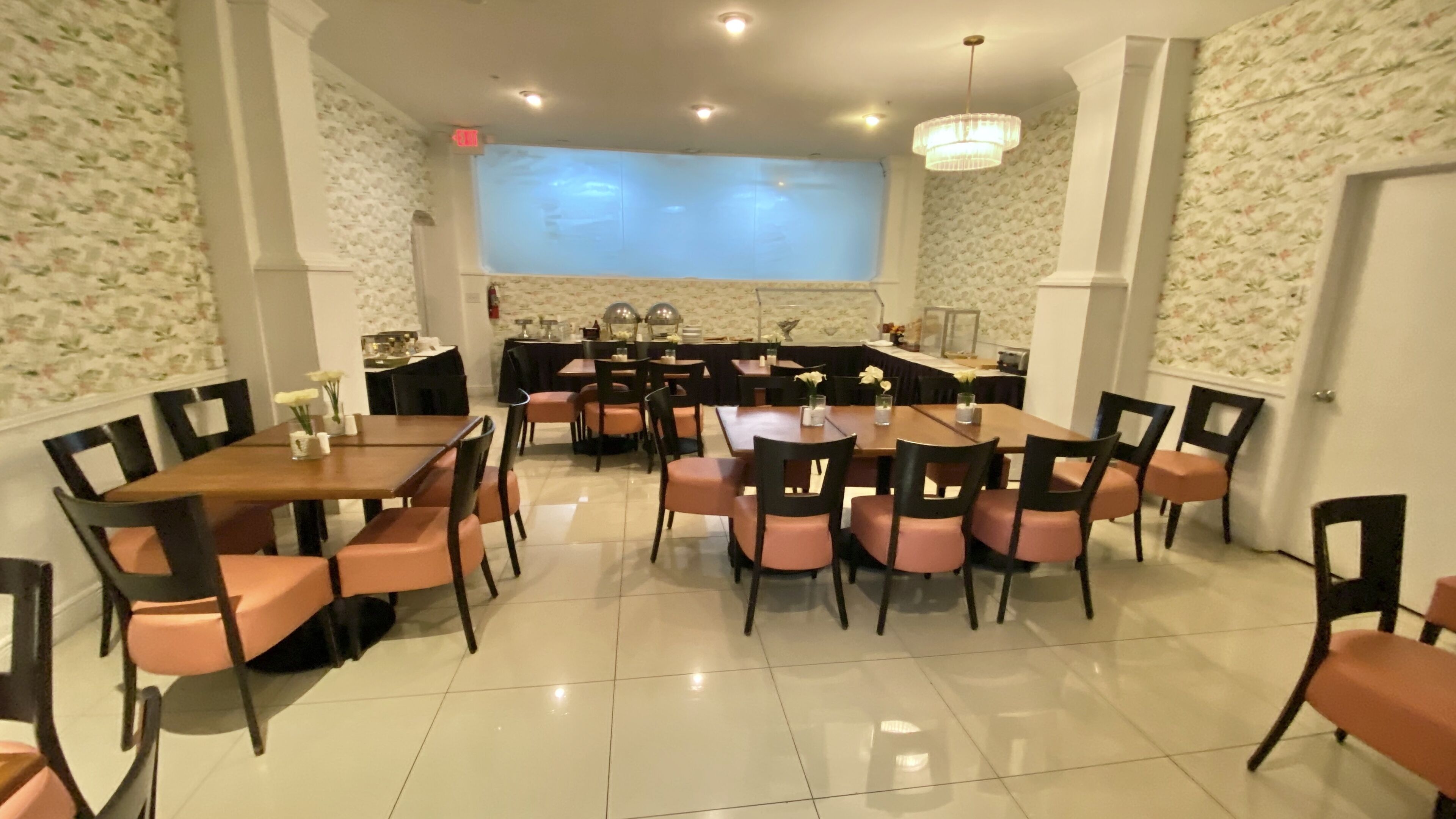 Un espace repas avec plusieurs tables et chaises, une cuisine à l’arrière-plan et un lustre.
