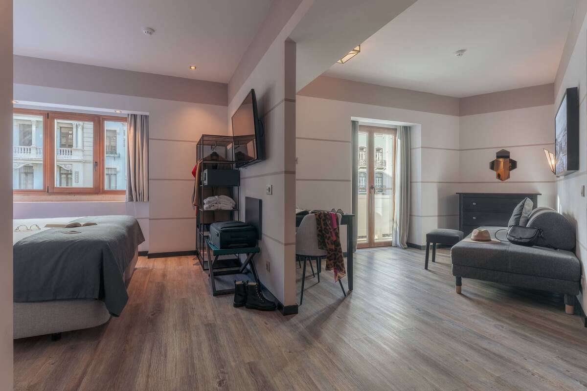 A modern hotel room with a bed, a desk, a chair, and a sofa.