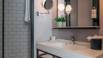 Une salle de bain moderne avec un lavabo blanc, deux miroirs fixés au mur, un porte-serviettes, une plante en pot et une bouteille d’huile moteur Castrol.
