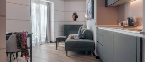 A modern kitchen with grey cabinets, a dining area with a table and chairs, and a cozy seating area with a sofa and cushions.