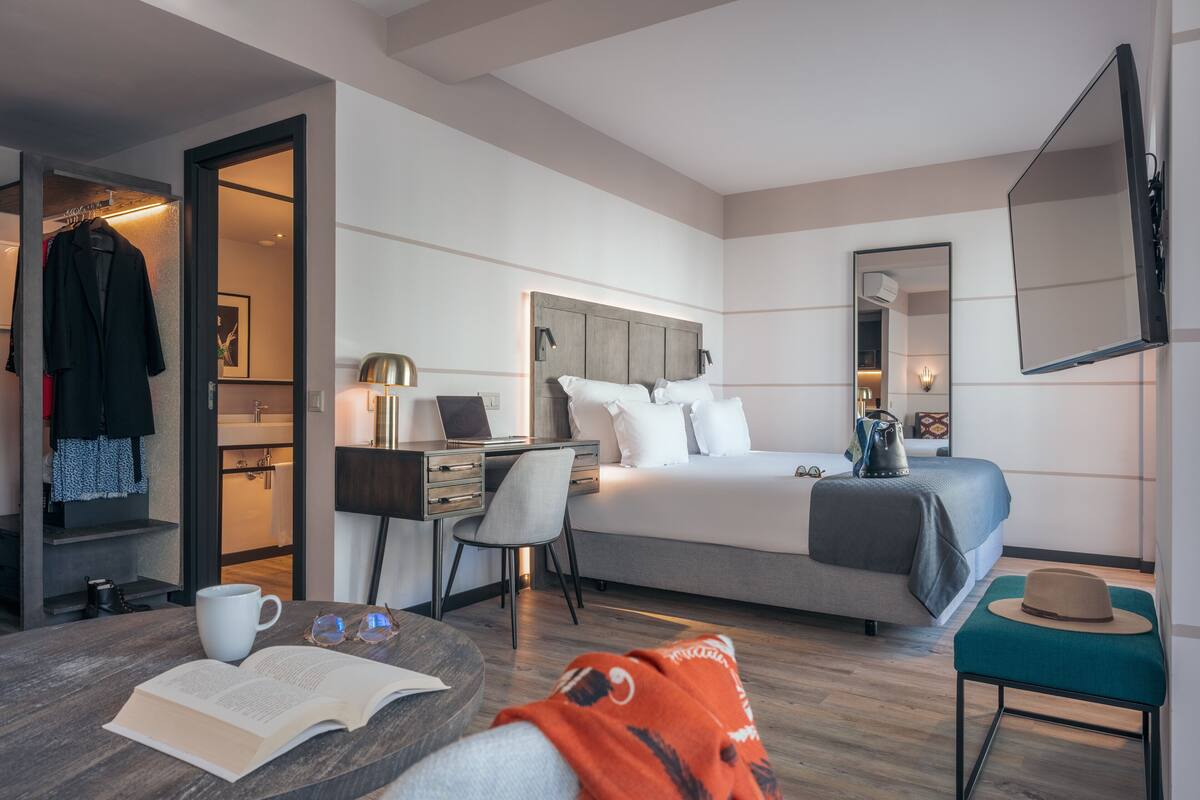 A modern hotel room with a bed, desk, chair, and a television.