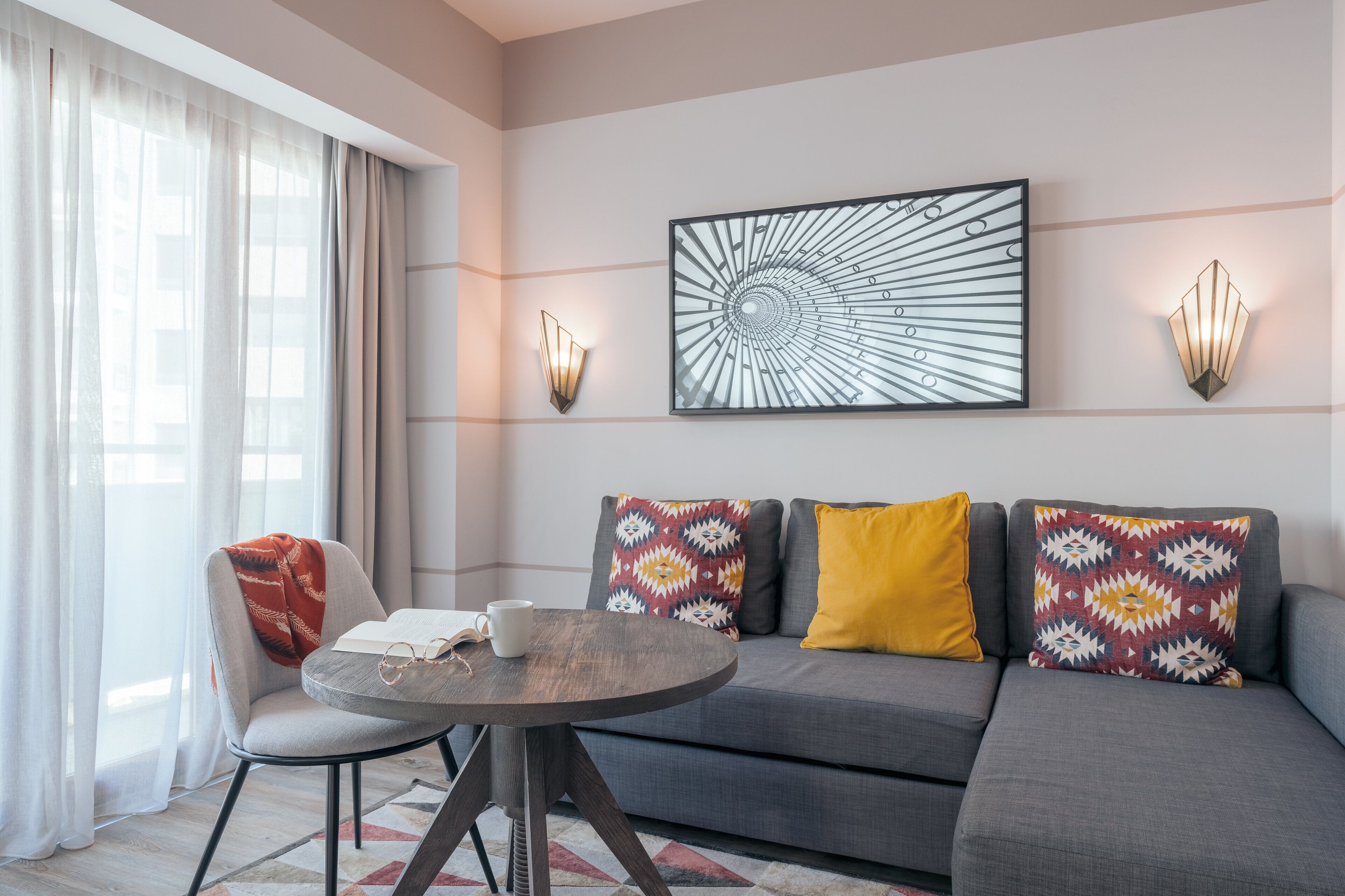 A modern living room with a grey sofa, patterned cushions, a round coffee table, and a framed abstract artwork on the wall.