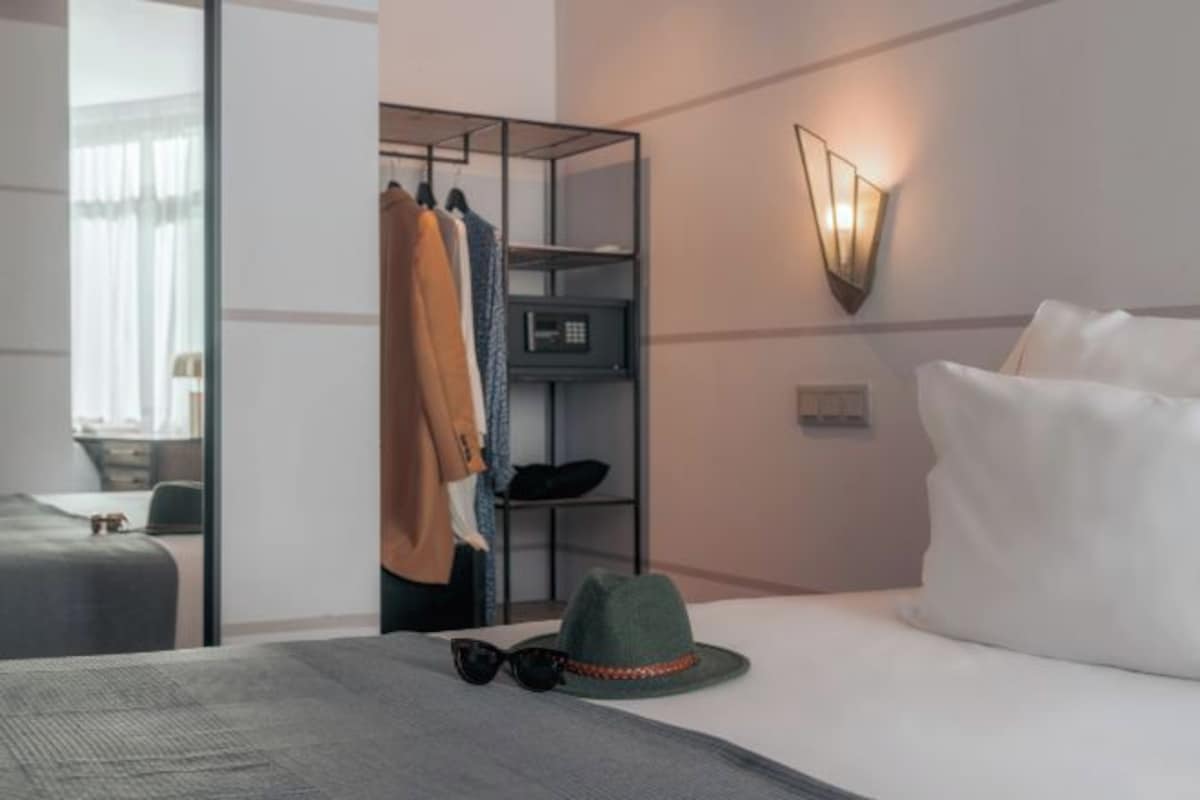 Una habitación de hotel con cama, armario, perchero e iluminación empotrada en la pared.