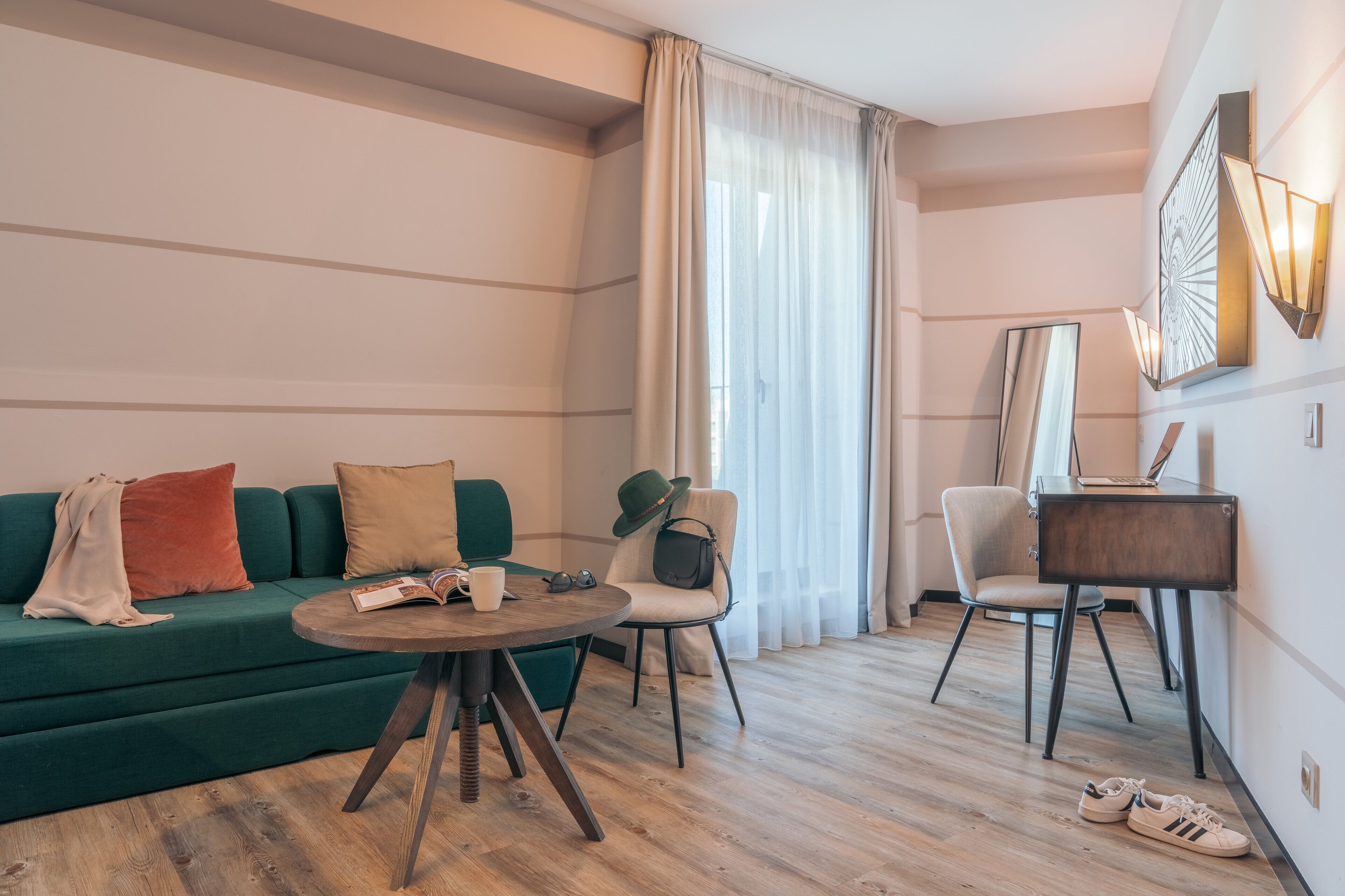 A modern living room with a green sofa, a round wooden coffee table, and a small desk with a chair.