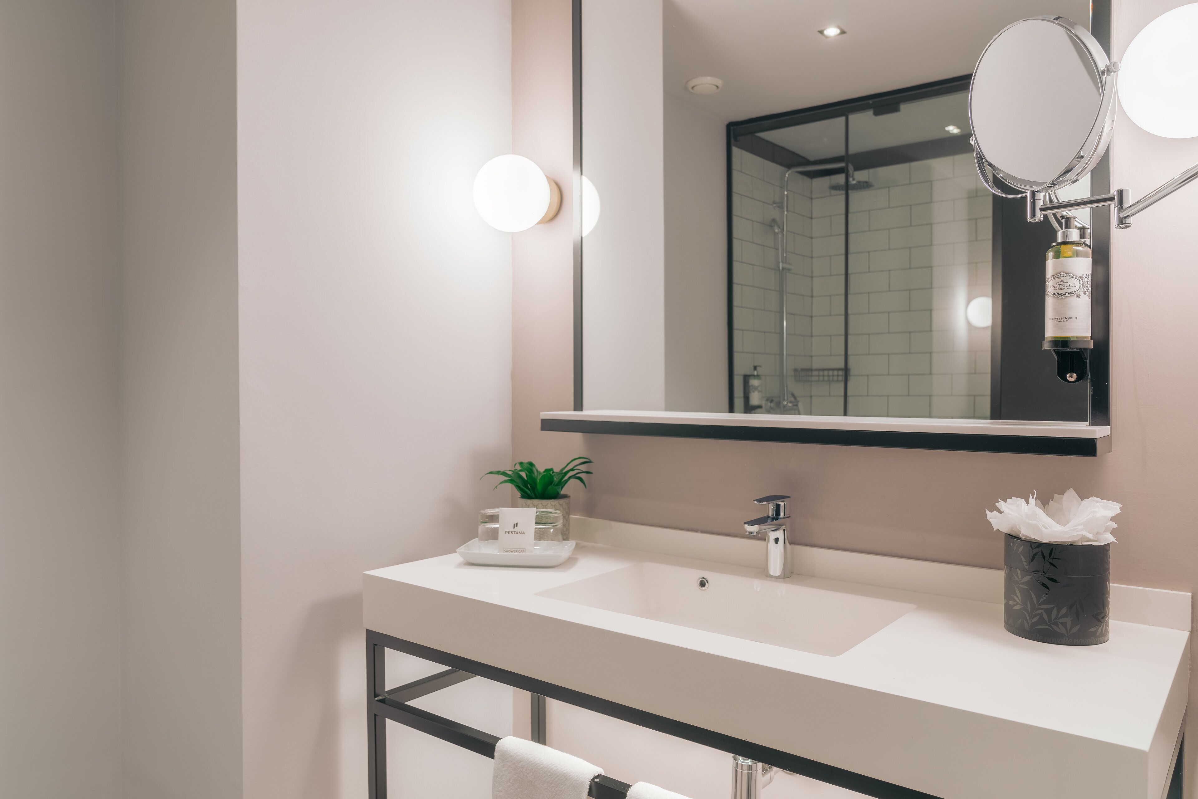 A modern bathroom with a white sink, a mirror, and a shower area.